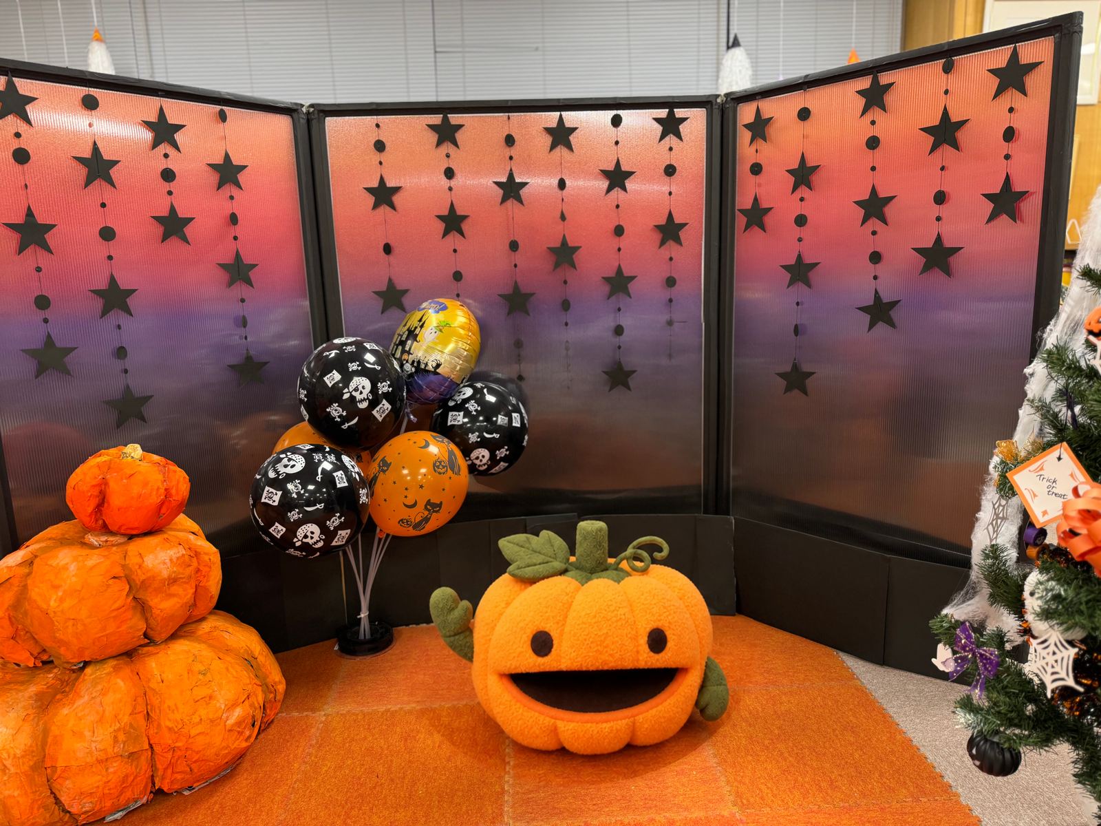 ハロウィンの風船とかぼちゃが並ぶフォトスポット。人物はかぼちゃのマスコットに置換
